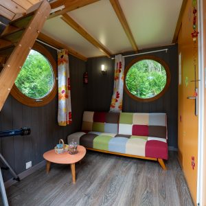Hébergement insolite à Champagne-Ardennes : cabane colorée avec fenêtres rondes et escalier en bois.