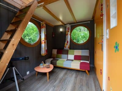 Hébergement insolite à Champagne-Ardennes : cabane colorée avec fenêtres rondes et escalier en bois.