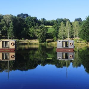 Hébergement insolite : cabanes flottantes sur un lac paisible, entourées de verdure.