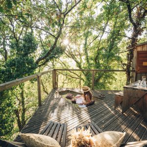 Cabane perchée dans les arbres, terrasse en bois entourée de verdure, ambiance paisible.