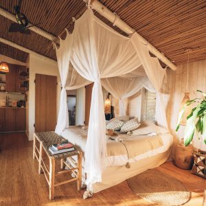 Chambre en cabane avec lit à baldaquin et décoration en bambou, ambiance chaleureuse.