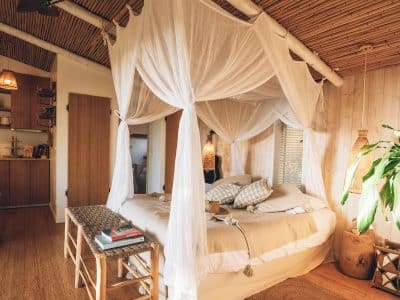 Chambre en cabane avec lit à baldaquin et décoration en bambou, ambiance chaleureuse.