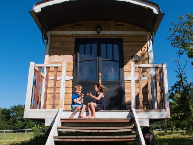 Roulotte en bois à Auvergne, avec des enfants jouant sur les marches ensoleillées.