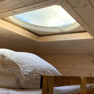 Cabane en bois avec un velux offrant une vue sur le ciel, ambiance cosy et naturelle.