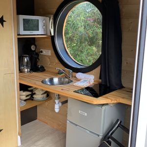 Hébergement insolite à Limousin : kitchenette moderne avec fenêtre ronde et décor bois.