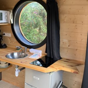 Hébergement insolite à Limousin : cuisine moderne avec fenêtre ronde et bois chaleureux.