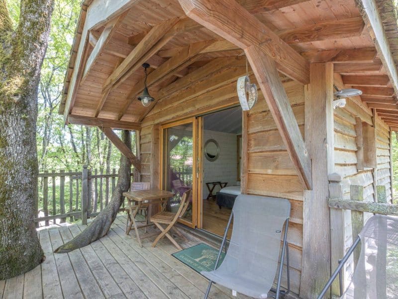 Cabane en bois avec terrasse, entourée de verdure et lumière naturelle.