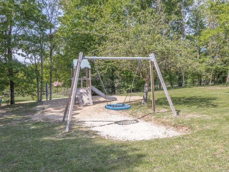 Aire de jeux dans un camping, avec balançoires et toboggan entourés darbres.