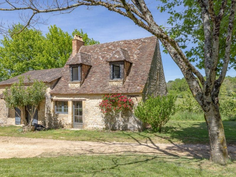 Charmante maison en pierre avec un toit en ardoise, entourée darbres verdoyants.