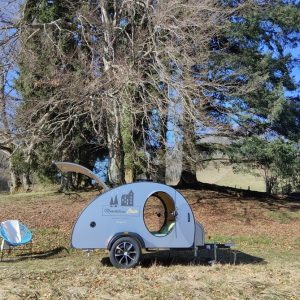 Hébergement insolite en roulotte, entouré darbres majestueux et de chaises confortables.