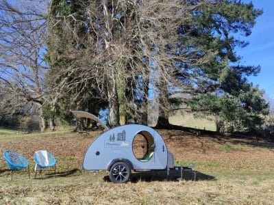 Hébergement insolite en roulotte, entouré darbres majestueux et de chaises confortables.