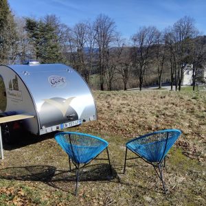 Hébergement insolite en Auvergne : une petite caravane argentée avec chaises colorées.