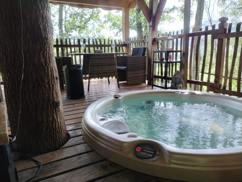 Cabane en bois avec jacuzzi sur une terrasse entourée darbres.