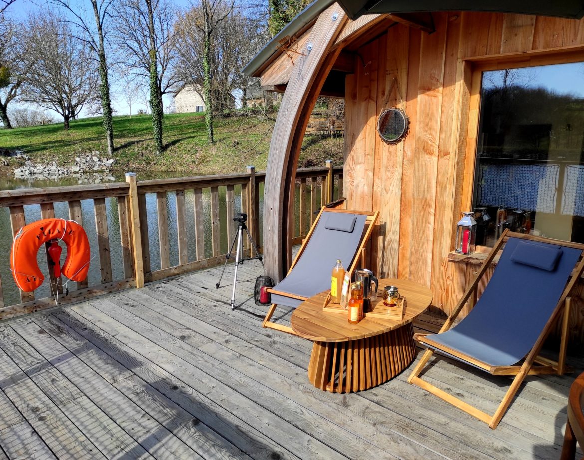 Hébergement insolite en bois au bord de leau, avec chaises longues et vue paisible.