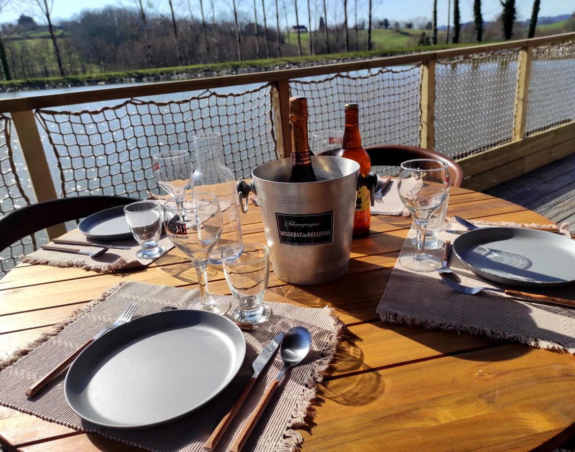 Table en bois avec vue sur leau, champagne prêt pour un séjour en cabane insolite.