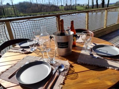Table en bois avec vue sur leau, champagne prêt pour un séjour en cabane insolite.