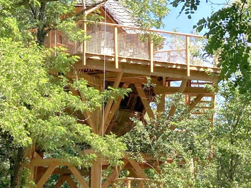 Cabane perchée dans les arbres, entourée de verdure luxuriante et lumineuse.