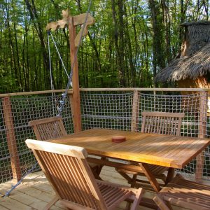 Cabane perchée en bois avec terrasse en bois et vue sur la forêt verdoyante.