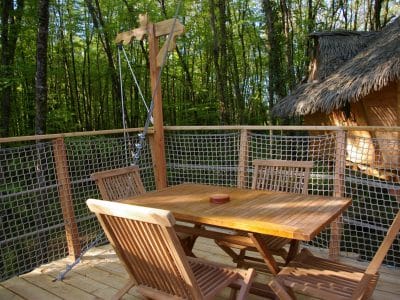 Cabane perchée en bois avec terrasse en bois et vue sur la forêt verdoyante.