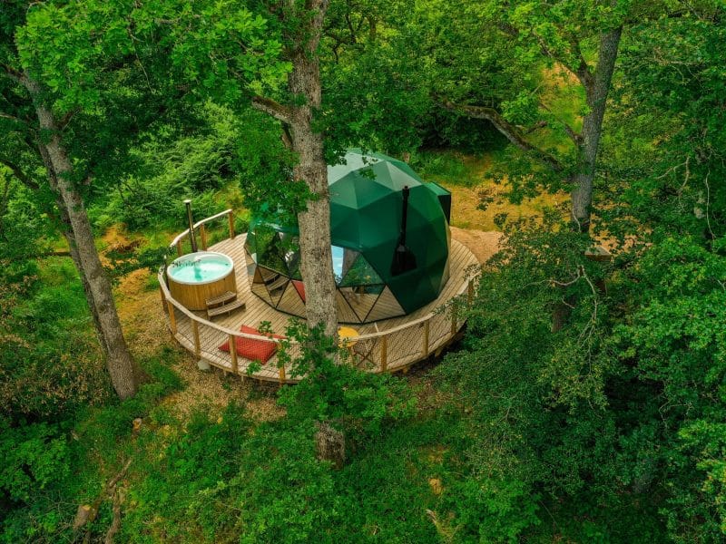 Dôme géodésique en pleine nature, avec jacuzzi sur la terrasse boisée.