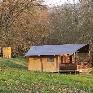 Tente safari en Limousin, entourée darbres, avec une terrasse en bois accueillante.