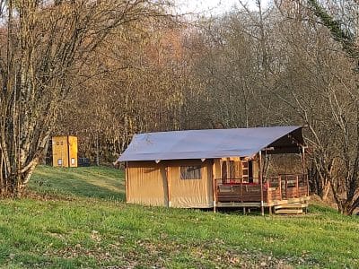 Tente safari en Limousin, entourée darbres, avec une terrasse en bois accueillante.