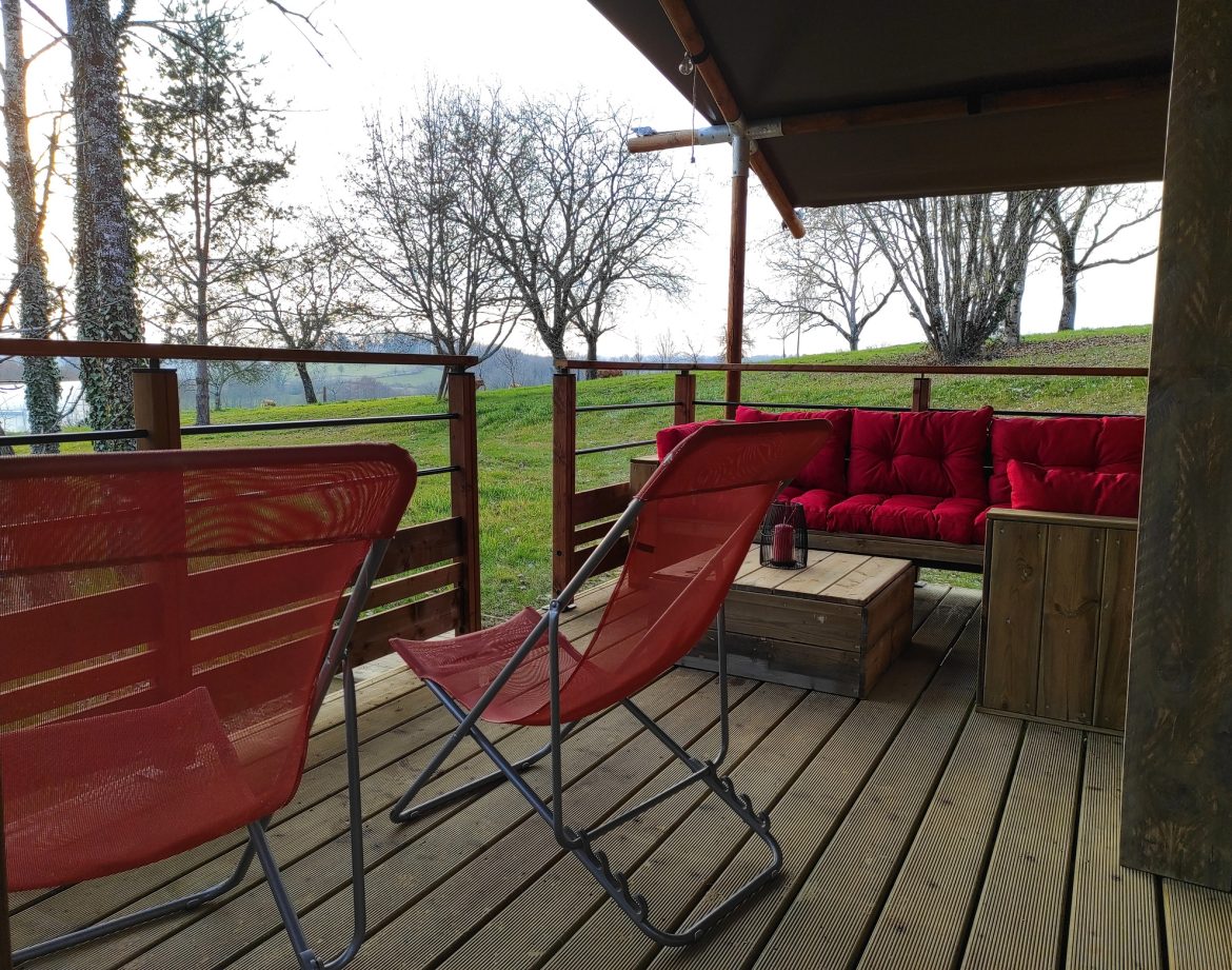 Tente lodge à Limousin avec terrasse en bois et canapé rouge confortable.