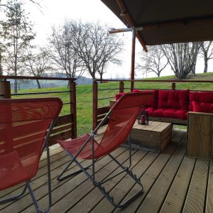 Tente lodge à Limousin avec terrasse en bois et canapé rouge confortable.