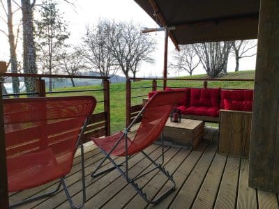 Tente lodge à Limousin avec terrasse en bois et canapé rouge confortable.