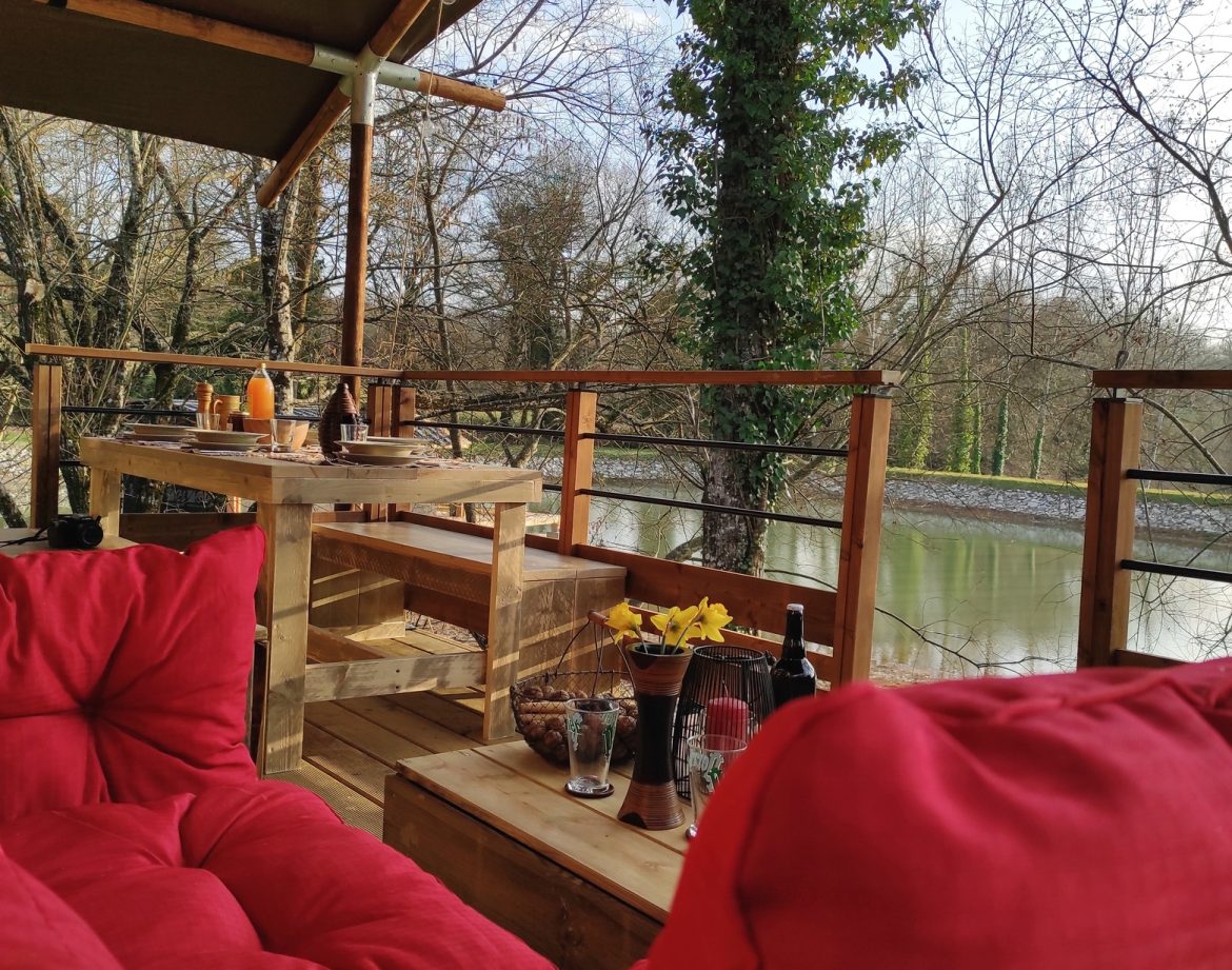 Hébergement insolite en cabane sur pilotis, avec vue sur la rivière et coussins rouges.