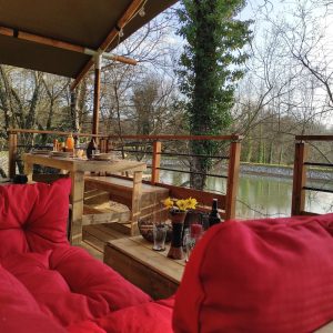 Hébergement insolite en cabane sur pilotis, avec vue sur la rivière et coussins rouges.