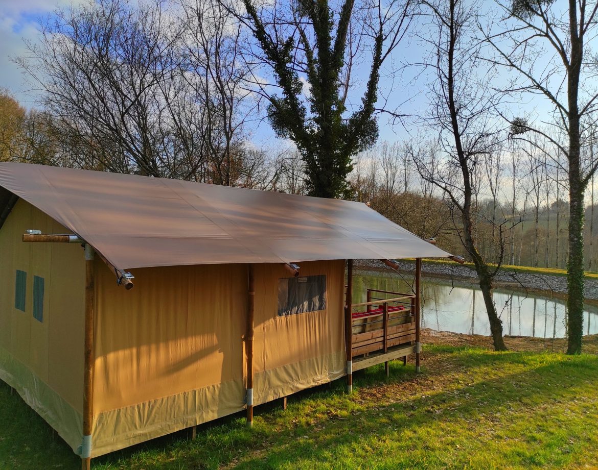 Tente safari en Limousin, entourée darbres et près dun étang paisible.