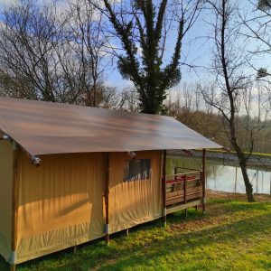 Tente safari en Limousin, entourée darbres et près dun étang paisible.