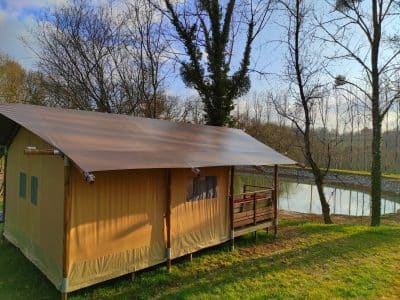 Tente safari en Limousin, entourée darbres et près dun étang paisible.