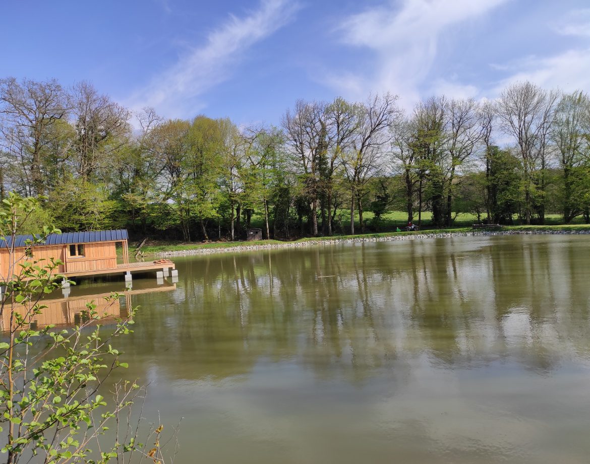 Cabane flottante au Limousin, entourée darbres verdoyants et dun lac paisible.