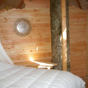 Cabane en bois dans les arbres, avec un lit douillet et un mur en bois clair.