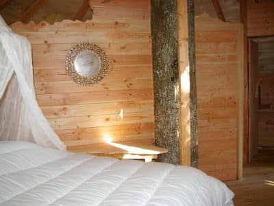 Cabane en bois dans les arbres, avec un lit douillet et un mur en bois clair.