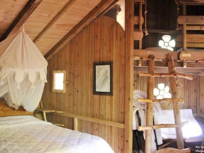 Cabane en bois avec lit suspendu et échelle en rondins, ambiance chaleureuse.