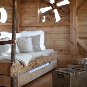 Cabane en bois avec lit douillet et décor naturel, ambiance chaleureuse et rustique.