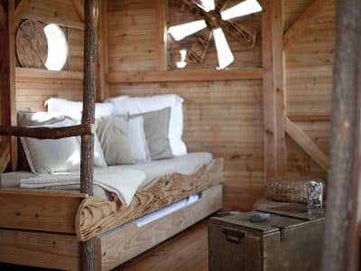 Cabane en bois avec lit douillet et décor naturel, ambiance chaleureuse et rustique.