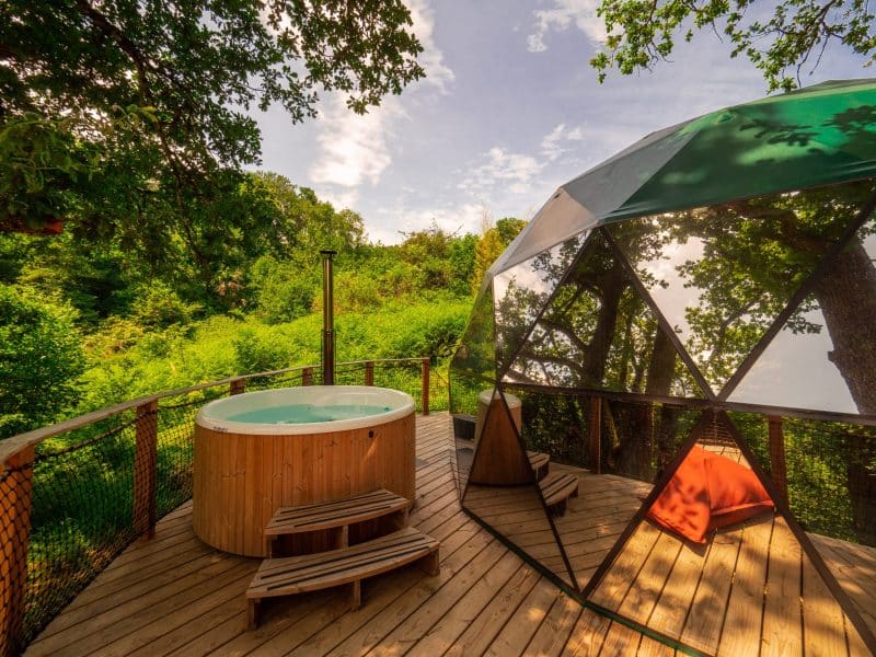 Dôme transparent avec jacuzzi, entouré de verdure, offrant une vue imprenable.