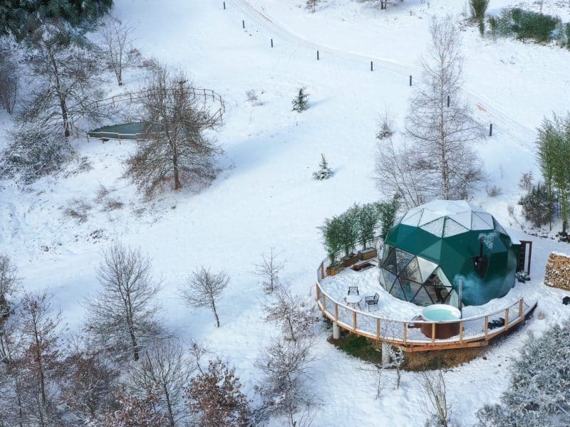 Dôme géodésique en pleine neige, avec terrasse et jacuzzi extérieur.