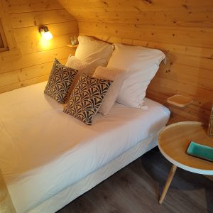 Chalet en bois cosy en Bourgogne, lit douillet avec coussins décoratifs.