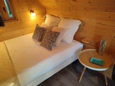 Chalet en bois cosy en Bourgogne, lit douillet avec coussins décoratifs.