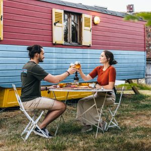 Hébergement insolite : une roulotte colorée avec un couple partageant un repas en plein air.