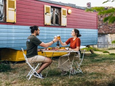 Hébergement insolite : une roulotte colorée avec un couple partageant un repas en plein air.