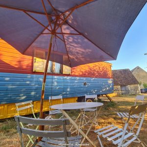 Charmant roulotte colorée avec parasol et mobilier de jardin dans un cadre paisible.