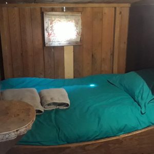 Cabane en bois avec un lit douillet et des draps turquoise. Ambiance chaleureuse.