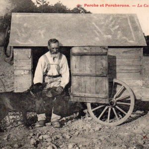 Cabane de berger en bois, avec un homme et un chien devant, dans un paysage rural.