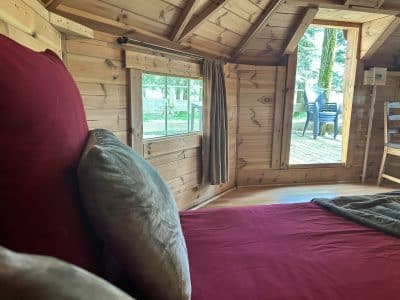 Intérieur dun hébergement insolite en bois, lit confortable et vue sur la nature.